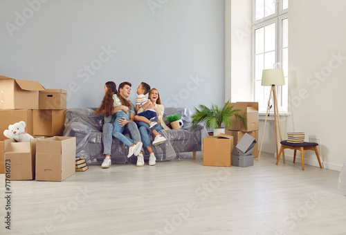 Happy in our new family home. Funny young Caucasian family is happy, having fun, laughing and hugging in house they just moved into. Family on sofa among cardboard boxes. Family relocation concept. photo