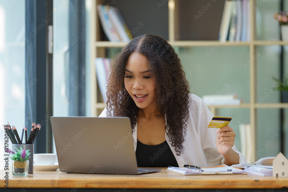 Portrait of young African-American woman holding credit card while enjoying online shopping at home office, copy space Portrait of young African-American woman holding credit card while enjoying online shopping at home office, copy space