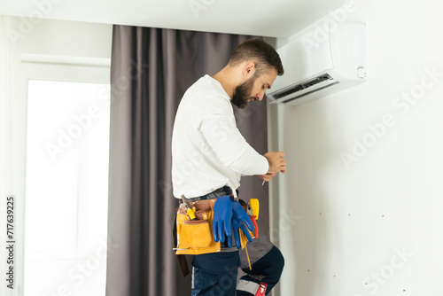 Male technician fixing air conditioner indoors.