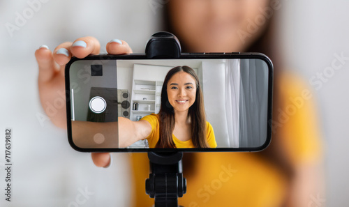 Smiling asian female vlogger creating content, using a smartphone mounted on tripod