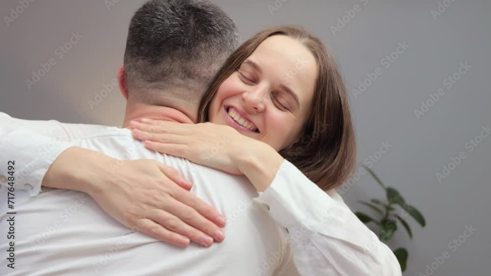 Extremely happy cheerful smiling positive woman wearing white shirt meeting her husband from work couple hugging each other with happy cheerful smiles and love Extremely happy cheerful smiling positive woman wearing white shirt meeting her husband from work couple hugging each other with happy cheerful smiles and love