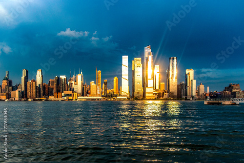 Wonderful skyline of New York and Big Apple seen from a viewpoint on the Hudson River, under a sunset and the sun's rays reflecting on the buildings.