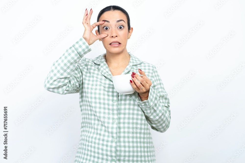 Beautiful young woman wearing green plaid pyjama and holding a cup keeping eyes opened to find a success opportunity. Beautiful young woman wearing green plaid pyjama and holding a cup keeping eyes opened to find a success opportunity.