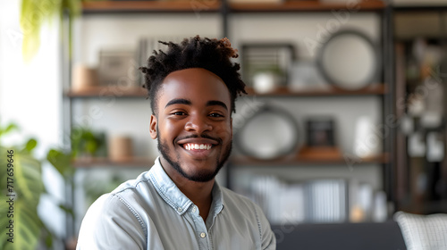 A happy, smiling man of African American descent in his twenties is facing the camera while standing in front of his home office backdrop. Black man smiling and self-assured as posing for a close-up h photo