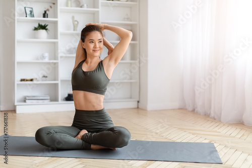 Fit asian woman making seated yoga tricep stretch while training at home