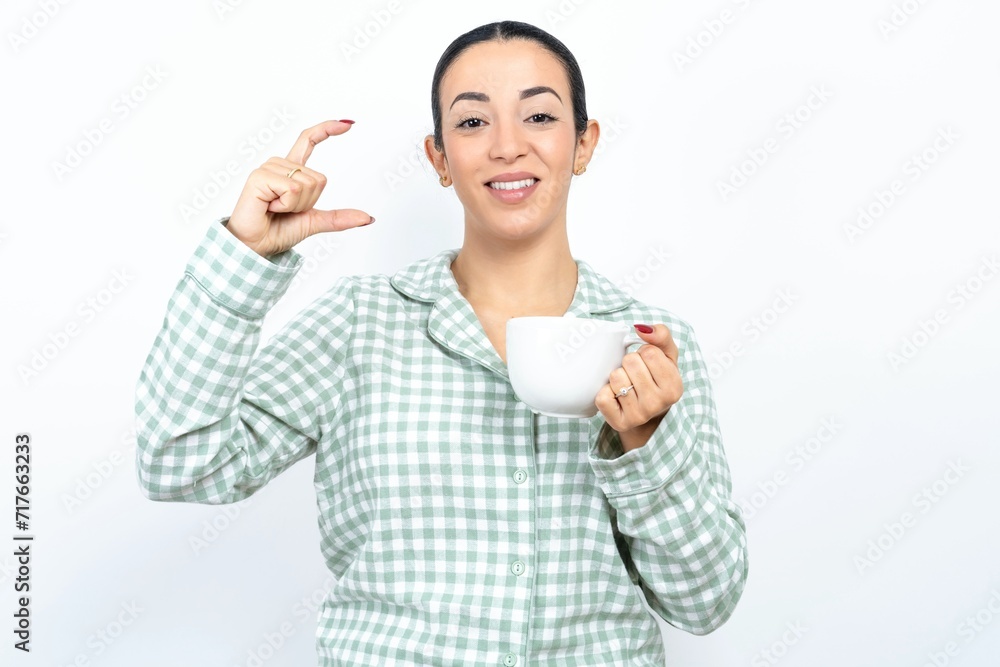 Beautiful young woman wearing green plaid pyjama smiling and confident gesturing with hand doing small size sign with fingers looking and the camera. Measure concept Beautiful young woman wearing green plaid pyjama smiling and confident gesturing with hand doing small size sign with fingers looking and the camera. Measure concept