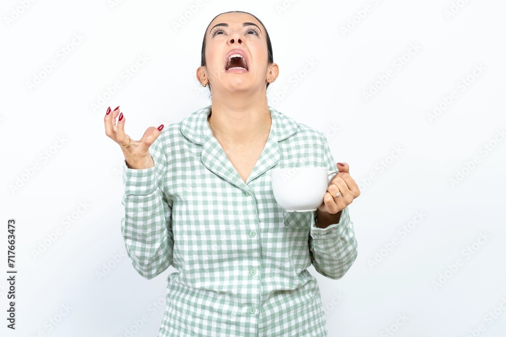 Beautiful young woman wearing green plaid pyjama crazy and mad shouting and yelling with aggressive expression and arms raised. Frustration concept. Beautiful young woman wearing green plaid pyjama crazy and mad shouting and yelling with aggressive expression and arms raised. Frustration concept.