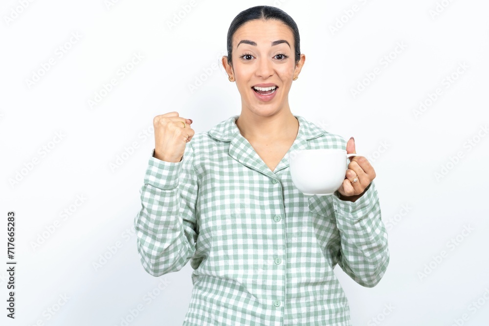 Obraz premium Beautiful young woman wearing green plaid pyjama celebrating surprised and amazed for success with arms raised and open eyes. Winner concept.