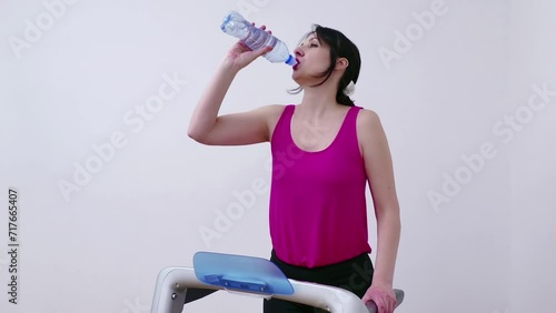 Young woman is exercising on a treadmill and drinking water to hydrate her body, Video Clip 4K