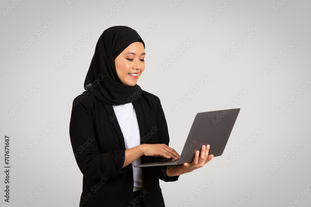 Engaged and smiling Muslim woman in a hijab and business attire working on a laptop Engaged and smiling Muslim woman in a hijab and business attire working on a laptop