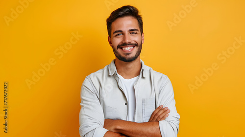 Rich, self-assured man standing alone with a smile against a yellow backdrop. Happy, attractive, ethnic man in a shirt glancing at a camera while posing for a portrait with his arms crossed photo
