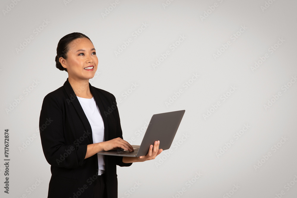 Asian businesswoman in a black blazer with a content smile working on a laptop Asian businesswoman in a black blazer with a content smile working on a laptop