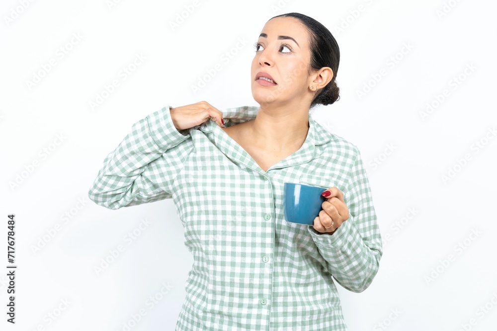 Beautiful young woman wearing green plaid pyjama and holding a cup stressed, anxious, tired and frustrated, pulling shirt neck, looking frustrated with problem Beautiful young woman wearing green plaid pyjama and holding a cup stressed, anxious, tired and frustrated, pulling shirt neck, looking frustrated with problem