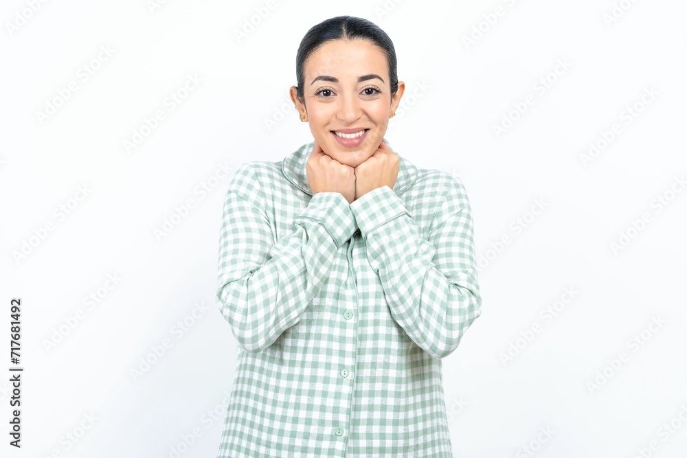 Satisfied Beautiful young woman wearing green plaid pyjama and holding a cup touches chin with both hands, smiles pleasantly, rejoices good day with lover Satisfied Beautiful young woman wearing green plaid pyjama and holding a cup touches chin with both hands, smiles pleasantly, rejoices good day with lover