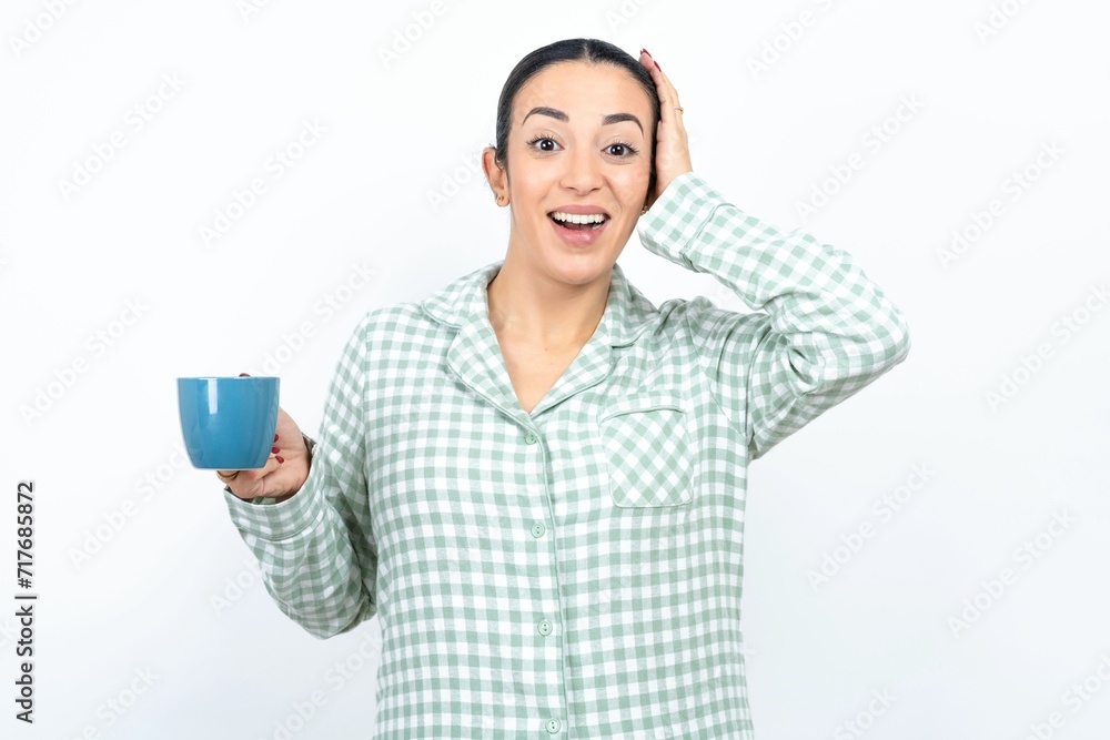 Shocked amazed surprised Beautiful young woman wearing green plaid pyjama and holding a cup hold hand offering proposition Shocked amazed surprised Beautiful young woman wearing green plaid pyjama and holding a cup hold hand offering proposition