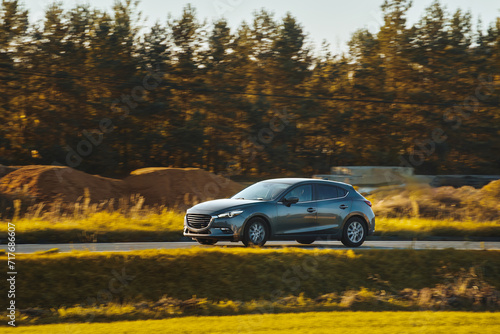 Car speeding in the countryside. Driving fast on a road surrounded by greenery in a modern hatchback. Side view of modern hatchback moving on the highway.