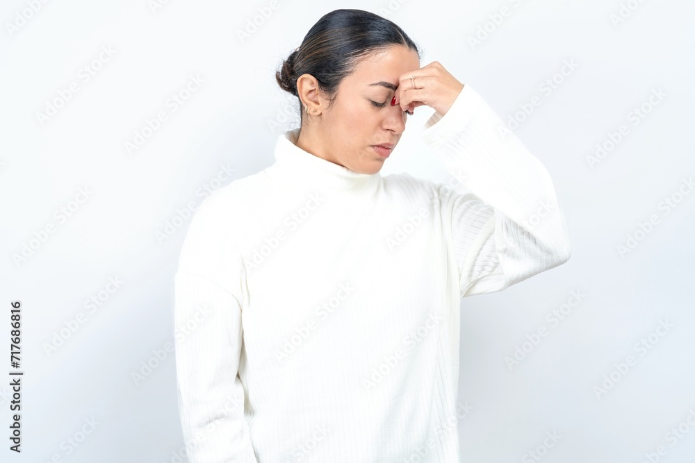 Sad Young beautiful woman wearing white turtleneck sweater suffering from headache holding hand on her face Sad Young beautiful woman wearing white turtleneck sweater suffering from headache holding hand on her face