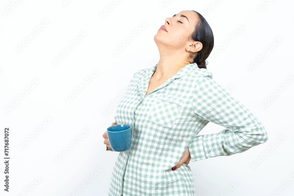 Beautiful young woman wearing green plaid pyjama and holding a cup got back pain Beautiful young woman wearing green plaid pyjama and holding a cup got back pain