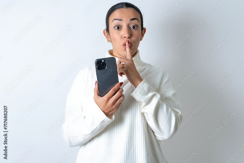 Young beautiful woman wearing white turtleneck sweater holding modern gadget ask not tell secrets Young beautiful woman wearing white turtleneck sweater holding modern gadget ask not tell secrets