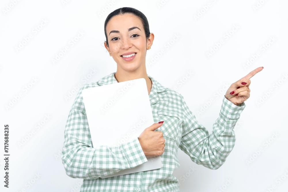 Beautiful young woman wearing green plaid pyjama and holding a cup holding laptop showing copy empty space ad Beautiful young woman wearing green plaid pyjama and holding a cup holding laptop showing copy empty space ad