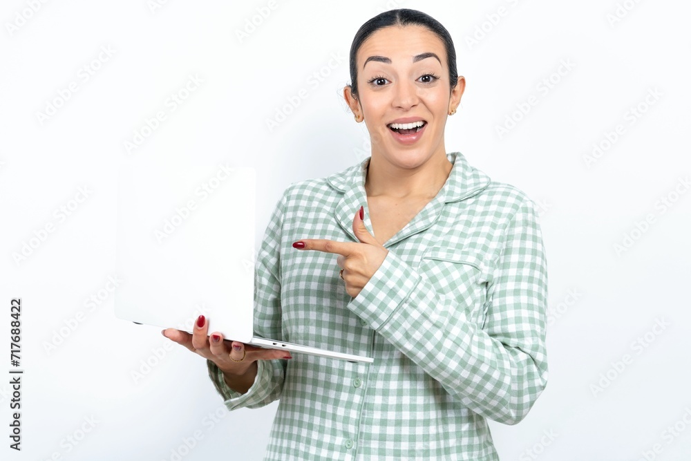 Shocked Beautiful young woman wearing green plaid pyjama and holding a cup pointing finger modern device Shocked Beautiful young woman wearing green plaid pyjama and holding a cup pointing finger modern device