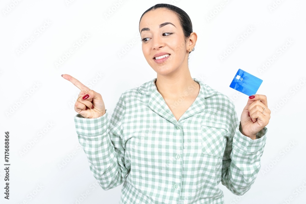 Curious smiling Beautiful young woman wearing green plaid pyjama and holding a cup showing plastic bank showing finger copyspace Curious smiling Beautiful young woman wearing green plaid pyjama and holding a cup showing plastic bank showing finger copyspace