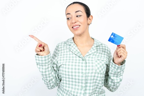 Curious smiling Beautiful young woman wearing green plaid pyjama and holding a cup showing plastic bank showing finger copyspace