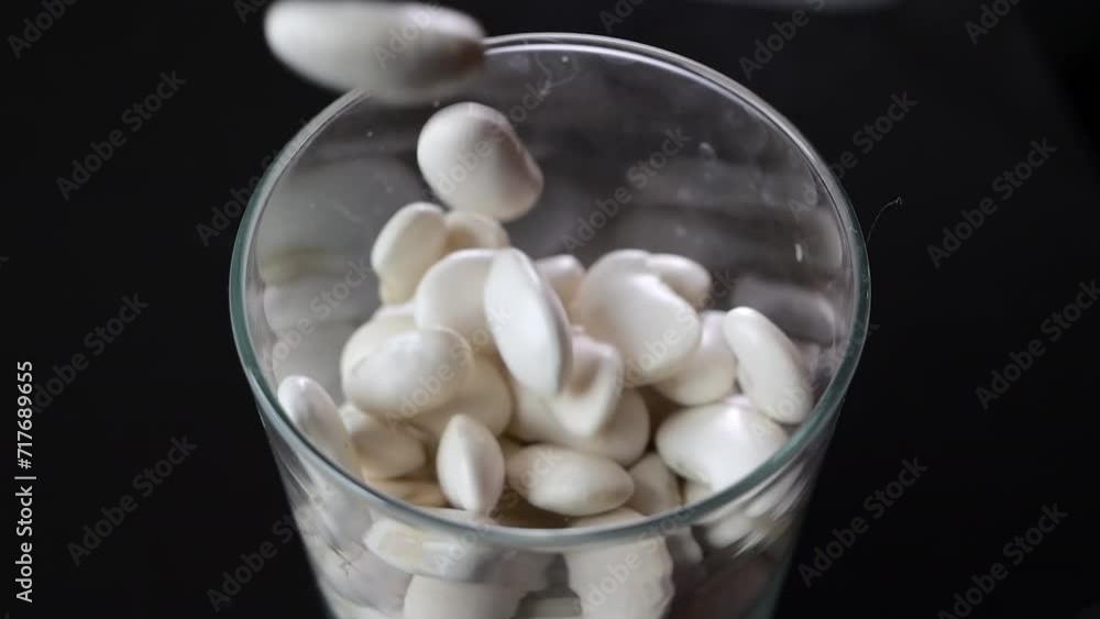 Delicate fall of white beans into a glass jar, in slow motion and against black, depicting the essence of a healthy pantry. Delicate fall of white beans into a glass jar, in slow motion and against black, depicting the essence of a healthy pantry.