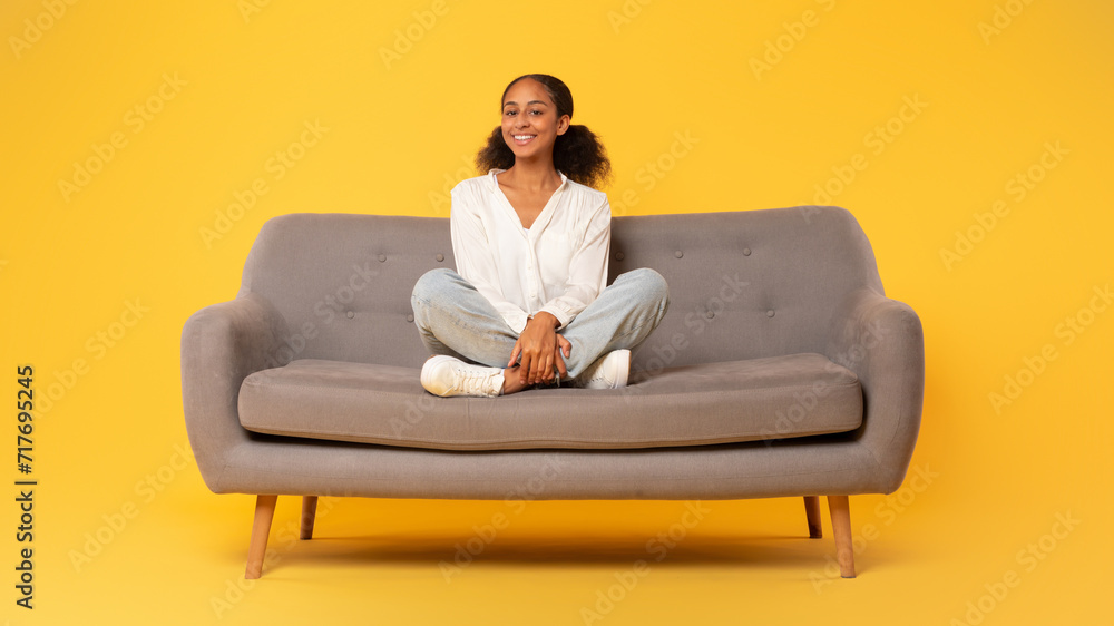 Cheerful african american teen girl sitting on sofa, yellow backdrop Cheerful african american teen girl sitting on sofa, yellow backdrop