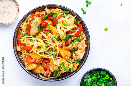 Stir fryed egg noodles with chicken, fresh pineapple, paprika, green onion, ginger, garlic, soy sauce and sesame seeds in bowl. Asian cuisine dish. White table background, top view