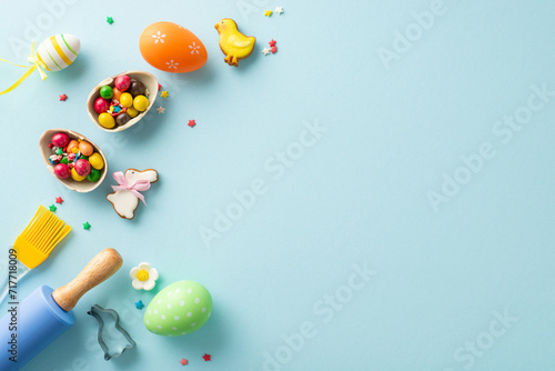 Easter anticipation at confectionery shop. Top view of table set for baking with roller-pin and brush. Playful pastry, sweet eggs, candies, sprinkles on light blue backdrop. Ideal for text placement