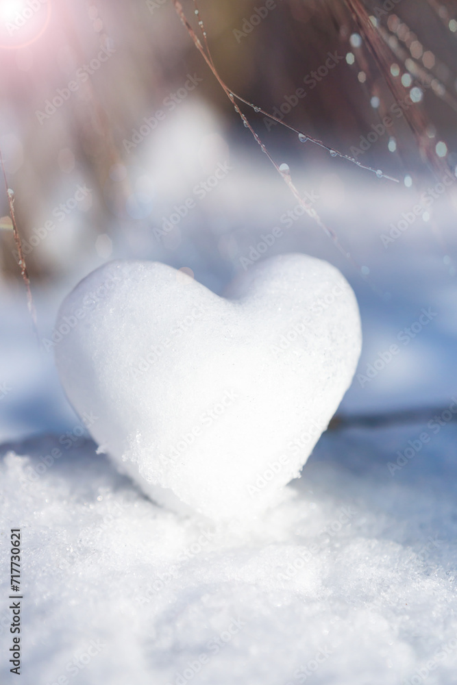 Fototapeta premium A snowy, tender heart against a winter background with beautiful bokeh.