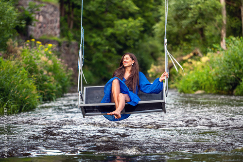 a joyful young woman swings on a rope swing across a fast-flowing river