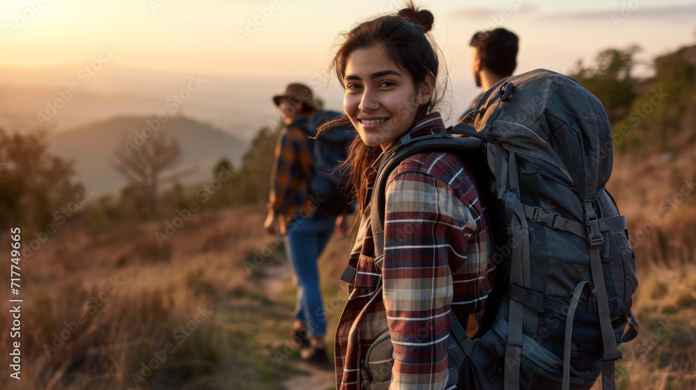 group of friends is hiking in the mountains at sunset, with a young woman in the foreground smiling at the camera