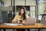 Attractive Asian businesswoman sitting using mobile phone at table in office