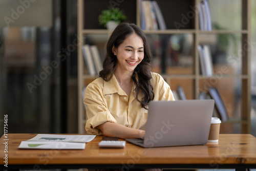 Attractive Asian businesswoman sitting work with laptop and documents at table in office.