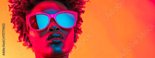 Stylish woman with afro hair wearing vibrant sunglasses against a radiant orange gradient.