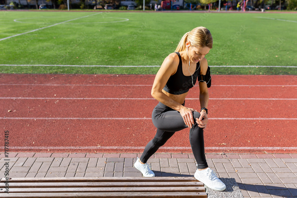 A fit woman pauses to look at her fitness tracker during a workout session on a sunny track field.