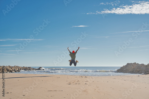 Happy man with arms in the air jumping on the beach - Successful hiker celebrating success on the shore - Lifestyle concept with young male walking the beach path.