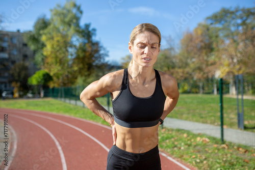 Focused woman in sportswear taking a break on the running track, showing determination and fitness drive.