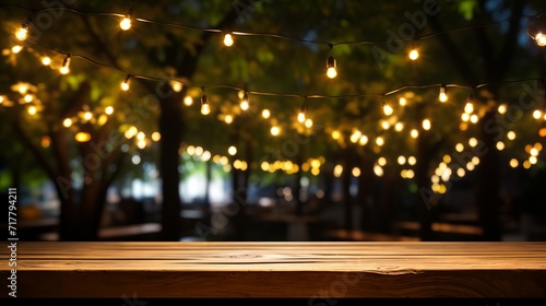 Empty wood table top with decorative outdoor string lights hanging on tree at night