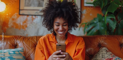 young woman laughing and using her smart phone while sitting on a couch