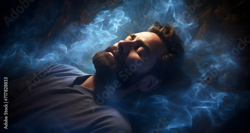 Dreaming beautiful thoughts - handsome bearded young male with eyes closed lying supine surrounded by wispy ethereal smoke appearing to be asleep or mediatating with a content expression on his face photo