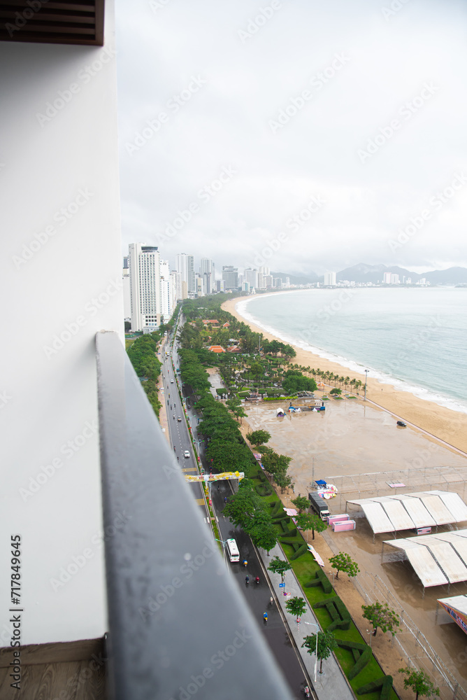 Balcony view aerial Nha Trang downtown, Tran Phu street along sandy shoreline beach park, concrete square, lush green tropical trees row high-rise hotel, apartment, office building background