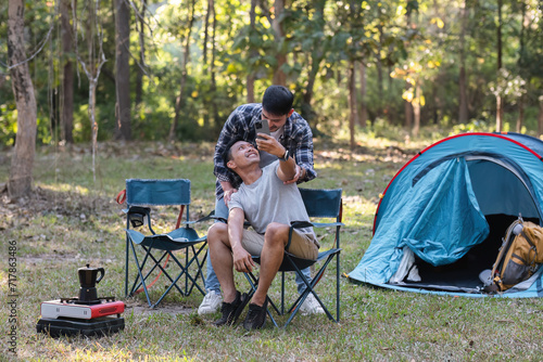 Asian LGBTQ couple tent in front of camp talking on smartphone in video chat or take a selfie