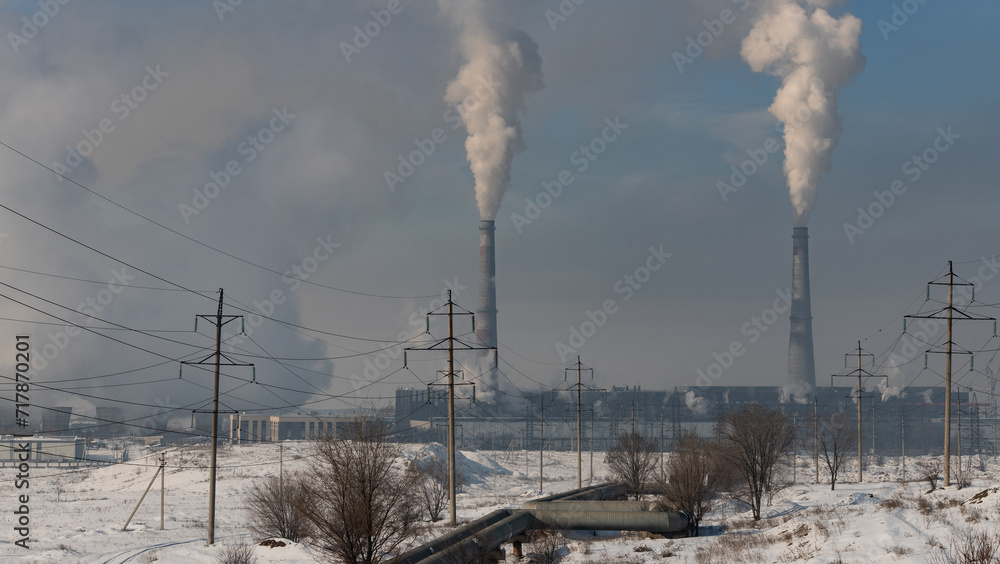 Smoking coal-fired power plant and high-voltage electricity transmission lines on a winter day