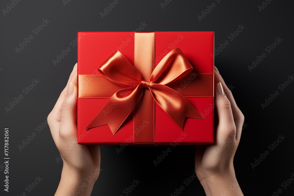 Top view of hands holding craft red paper gift box with ribbon bow on isolated black background. Generated AI. Top view of hands holding craft red paper gift box with ribbon bow on isolated black background. Generated AI.