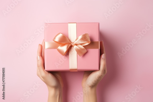 Top view of hands holding craft paper gift box with ribbon bow on isolated pastel blue background. Generated AI. © jirayut