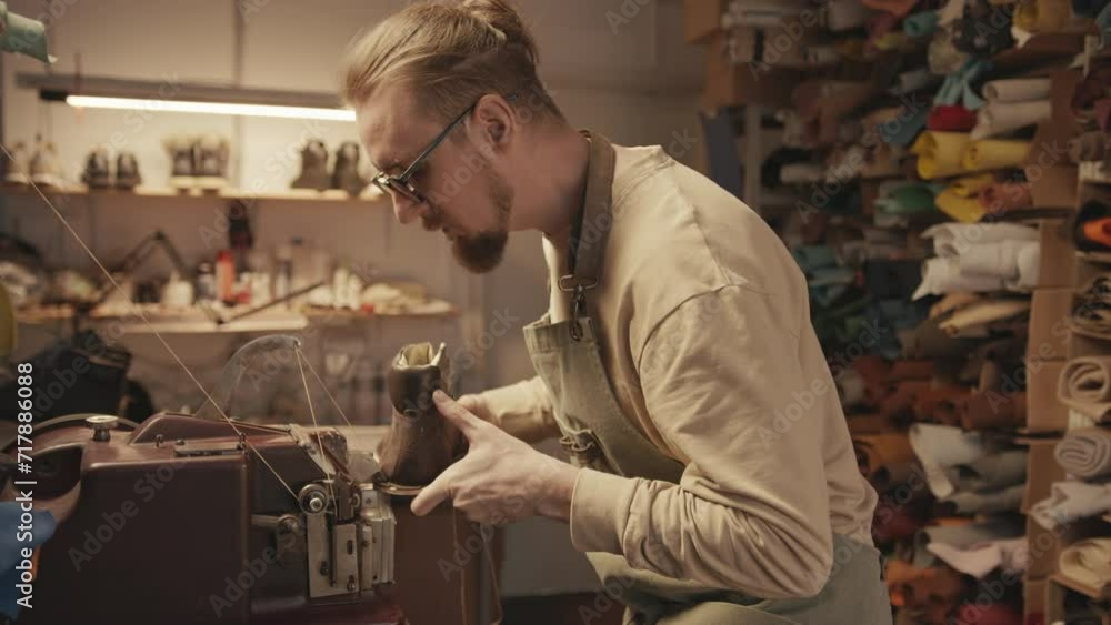 Side view of young shoemaker finishing handmade leather footwear with stitching machine in workshop Side view of young shoemaker finishing handmade leather footwear with stitching machine in workshop