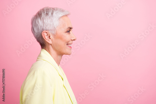 Side profile view shot of cheerful businesswoman in yellow jacket looking empty space formal haircut isolated on pink color background